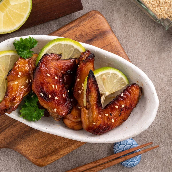 Kızarmış tatlı soslu teriyaki tavuk kanatlarının üst görüntüsü gri masa arkasında beyaz bir tabakta..