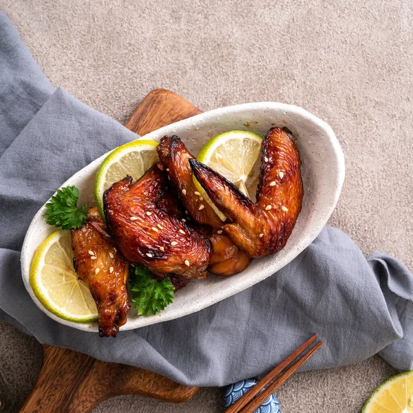 Kızarmış tatlı soslu teriyaki tavuk kanatlarının üst görüntüsü gri masa arkasında beyaz bir tabakta..