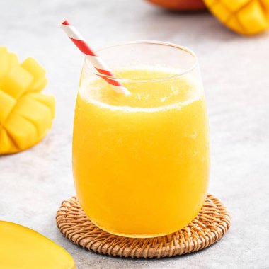 Taze nefis mango suyu. Gri masa arkasında kağıt kamışla cam bir fincanda buzlu içecek tasarımı yakın plan..