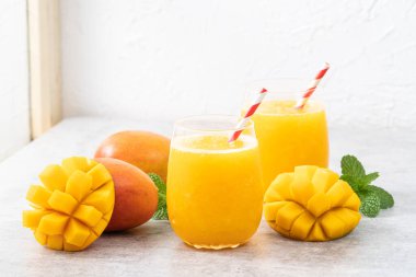 Taze nefis mango suyu. Gri masa arkasında kağıt kamışla cam bir fincanda buzlu içecek tasarımı yakın plan..