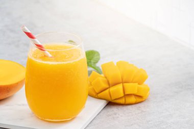 Taze nefis mango suyu. Gri masa arkasında kağıt kamışla cam bir fincanda buzlu içecek tasarımı yakın plan..