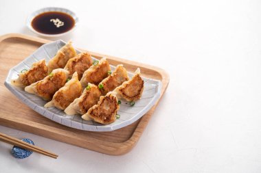 Tayvan ve Japon usulü kızarmış gyoza, beyaz masa arkasında soya sosu olan bir tabakta jiaozi yemeği yiyorlar..
