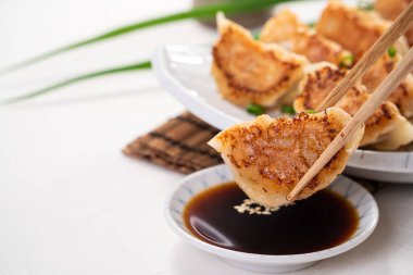 Tayvan ve Japon usulü kızarmış gyoza, beyaz masa arkasında soya sosu olan bir tabakta jiaozi yemeği yiyorlar..