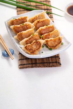 Tayvan ve Japon usulü kızarmış gyoza, beyaz masa arkasında soya sosu olan bir tabakta jiaozi yemeği yiyorlar..