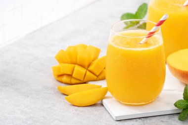 Taze nefis mango suyu. Gri masa arkasında kağıt kamışla cam bir fincanda buzlu içecek tasarımı yakın plan..