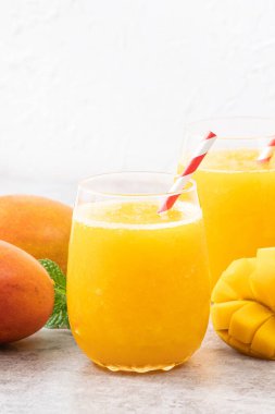 Taze nefis mango suyu. Gri masa arkasında kağıt kamışla cam bir fincanda buzlu içecek tasarımı yakın plan..