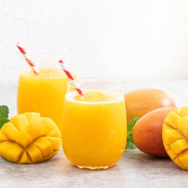 Taze nefis mango suyu. Gri masa arkasında kağıt kamışla cam bir fincanda buzlu içecek tasarımı yakın plan..