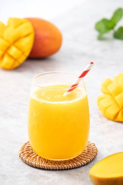 Taze nefis mango suyu. Gri masa arkasında kağıt kamışla cam bir fincanda buzlu içecek tasarımı yakın plan..