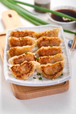 Tayvan ve Japon usulü kızarmış gyoza, beyaz masa arkasında soya sosu olan bir tabakta jiaozi yemeği yiyorlar..