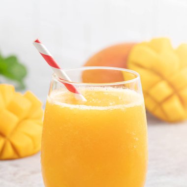 Taze nefis mango suyu. Gri masa arkasında kağıt kamışla cam bir fincanda buzlu içecek tasarımı yakın plan..