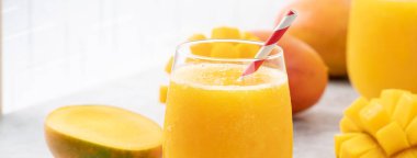 Taze nefis mango suyu. Gri masa arkasında kağıt kamışla cam bir fincanda buzlu içecek tasarımı yakın plan..