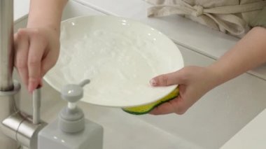 Kadın ev hanımı bulaşıkları yıkama süngeri ve bulaşık makinesiyle yıkıyor..