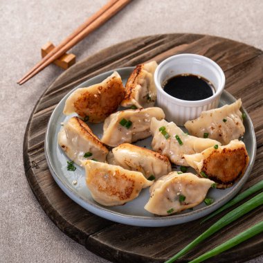 Tayvan ve Japon usulü kızarmış gyoza, gri masa arkasında soya sosu olan bir tabakta jiaozi yemeği yiyorlar..