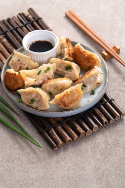 Tayvan ve Japon usulü kızarmış gyoza, gri masa arkasında soya sosu olan bir tabakta jiaozi yemeği yiyorlar..