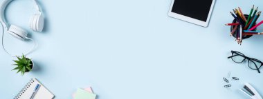 Çevrimiçi öğrenim tasarımı. Tabletli, kulaklıklı ve mavi masa arkaplanlı öğrenci tablosunun üst görünümü.