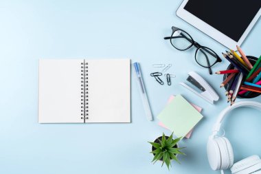 Çevrimiçi öğrenim tasarımı. Tabletli, kulaklıklı ve mavi masa arkaplanlı öğrenci tablosunun üst görünümü.