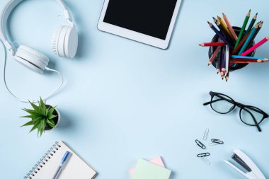 Çevrimiçi öğrenim tasarımı. Tabletli, kulaklıklı ve mavi masa arkaplanlı öğrenci tablosunun üst görünümü.