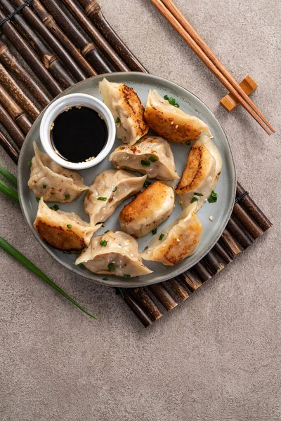 Tayvan ve Japon usulü kızarmış gyoza, gri masa arkasında soya sosu olan bir tabakta jiaozi yemeği yiyorlar..