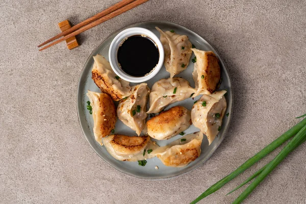 Tayvan ve Japon usulü kızarmış gyoza, gri masa arkasında soya sosu olan bir tabakta jiaozi yemeği yiyorlar..