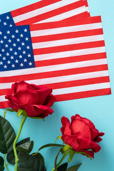 Concept of U.S Independence day or Memorial day. National flag over blue table background with red rose.