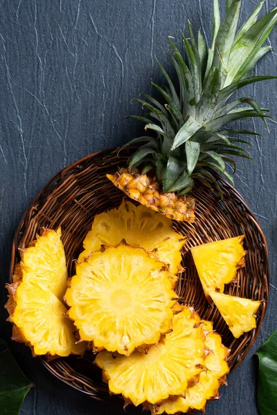 Top view of fresh cut pineapple with tropical leaves on dark blue background.