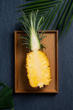 Koyu mavi arka planda tropikal yapraklı taze kesilmiş ananas manzarası.
