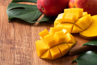 Mango. Taze olgun mango meyvelerini koyu ahşap masa zemininde yeşil yapraklarla kaplayın..