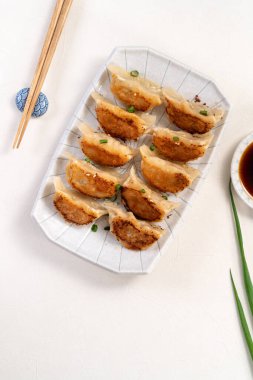 Tayvan ve Japon usulü kızarmış gyoza, beyaz masa arkasında soya sosu olan bir tabakta jiaozi yemeği yiyorlar..