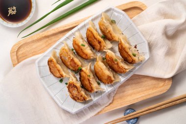 Tayvan ve Japon usulü kızarmış gyoza, beyaz masa arkasında soya sosu olan bir tabakta jiaozi yemeği yiyorlar..