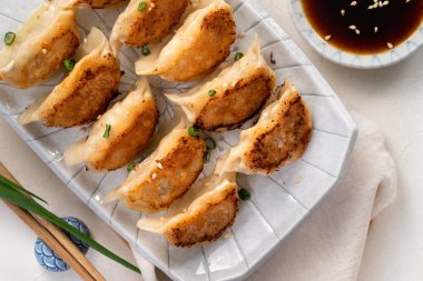 Tayvan ve Japon usulü kızarmış gyoza, beyaz masa arkasında soya sosu olan bir tabakta jiaozi yemeği yiyorlar..