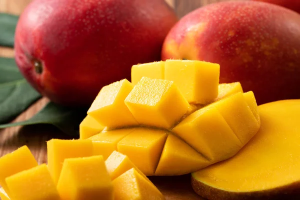 Mango. Close up of fresh ripe mango fruit with leaves over dark wooden table background with green leaves.