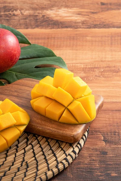 Mango. Close up of fresh ripe mango fruit with leaves over dark wooden table background with green leaves.