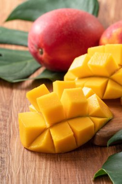 Mango. Taze olgun mango meyvelerini koyu ahşap masa zemininde yeşil yapraklarla kaplayın..