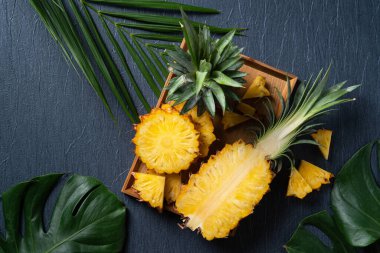 Koyu mavi arka planda tropikal yapraklı taze kesilmiş ananas manzarası.