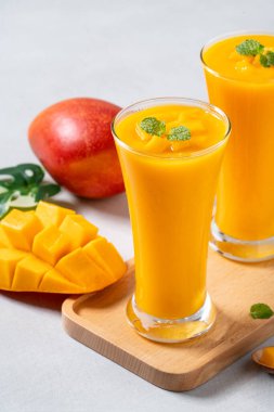 Taze nefis mango suyu. Smoothie soğuk içeceği cam bardakta gri masa arkasında cam pipetle yakın plan konsepti..
