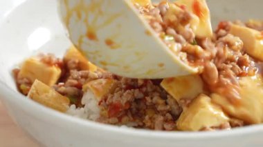 Pouring stir-fried mapo tofu with hot spicy sauce over white rice in a bowl at home