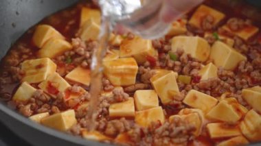 Cooking Mapo tofu. Homemade stir-frying tofu with hot spicy sauce in a pot at home.
