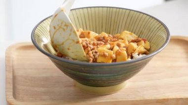 Pouring stir-fried mapo tofu with hot spicy sauce over white rice in a bowl at home