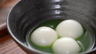 Close up of Matcha big tangyuan (tang yuan) with sweet matcha soup in a black bowl on table background for festival food.