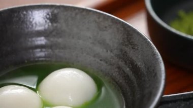 Close up of Matcha big tangyuan (tang yuan) with sweet matcha soup in a black bowl on table background for festival food.