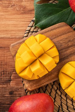 Taze olgun mango meyvelerinin en üst görüntüsü. Koyu ahşap masa arkasında yapraklar var..