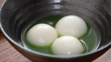 Close up of Matcha big tangyuan (tang yuan) with sweet matcha soup in a black bowl on table background for festival food.