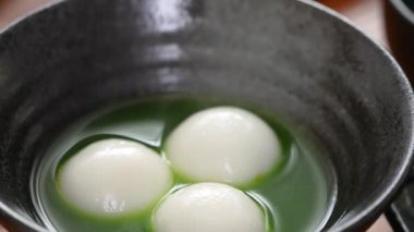 Close up of Matcha big tangyuan (tang yuan) with sweet matcha soup in a black bowl on table background for festival food.