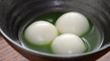 Close up of Matcha big tangyuan (tang yuan) with sweet matcha soup in a black bowl on table background for festival food.