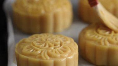 Brushing egg liquid on moon cake pastry surface before baking for Mid-Autumn Festival food concept.