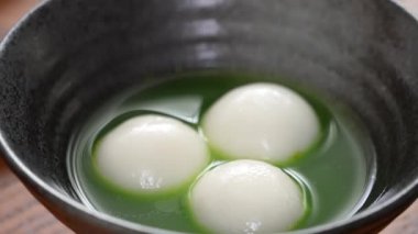 Close up of Matcha big tangyuan (tang yuan) with sweet matcha soup in a black bowl on table background for festival food.