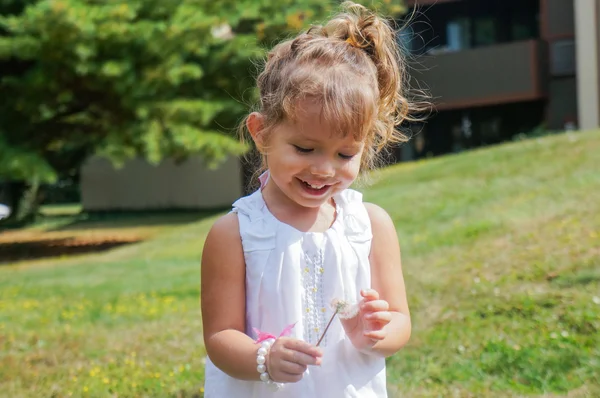 Cute baby girl is blowing a dandelion — Stock Photo, Image