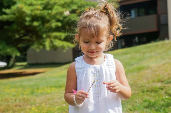 Cute baby girl is blowing a dandelion — Stock Photo, Image