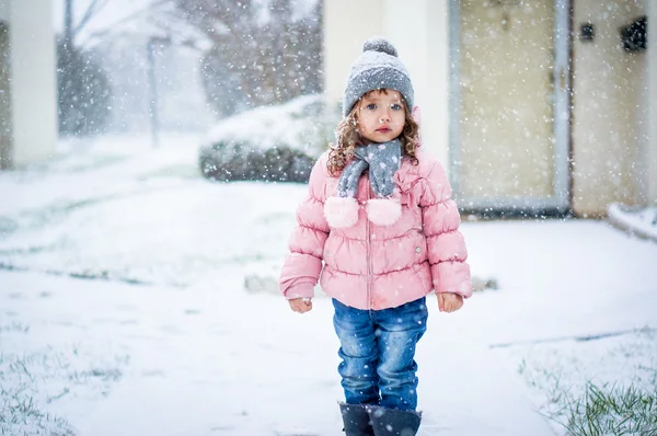 Söt baby flicka i rosa jackan och grå hatt njuter första snö b — Stockfoto