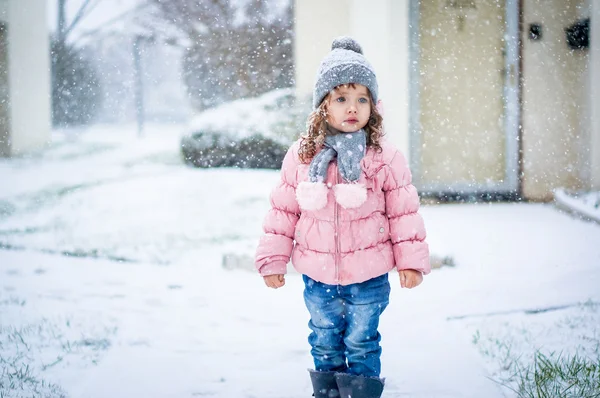 Söt baby flicka i rosa jackan och grå hatt njuter första snö b — Stockfoto